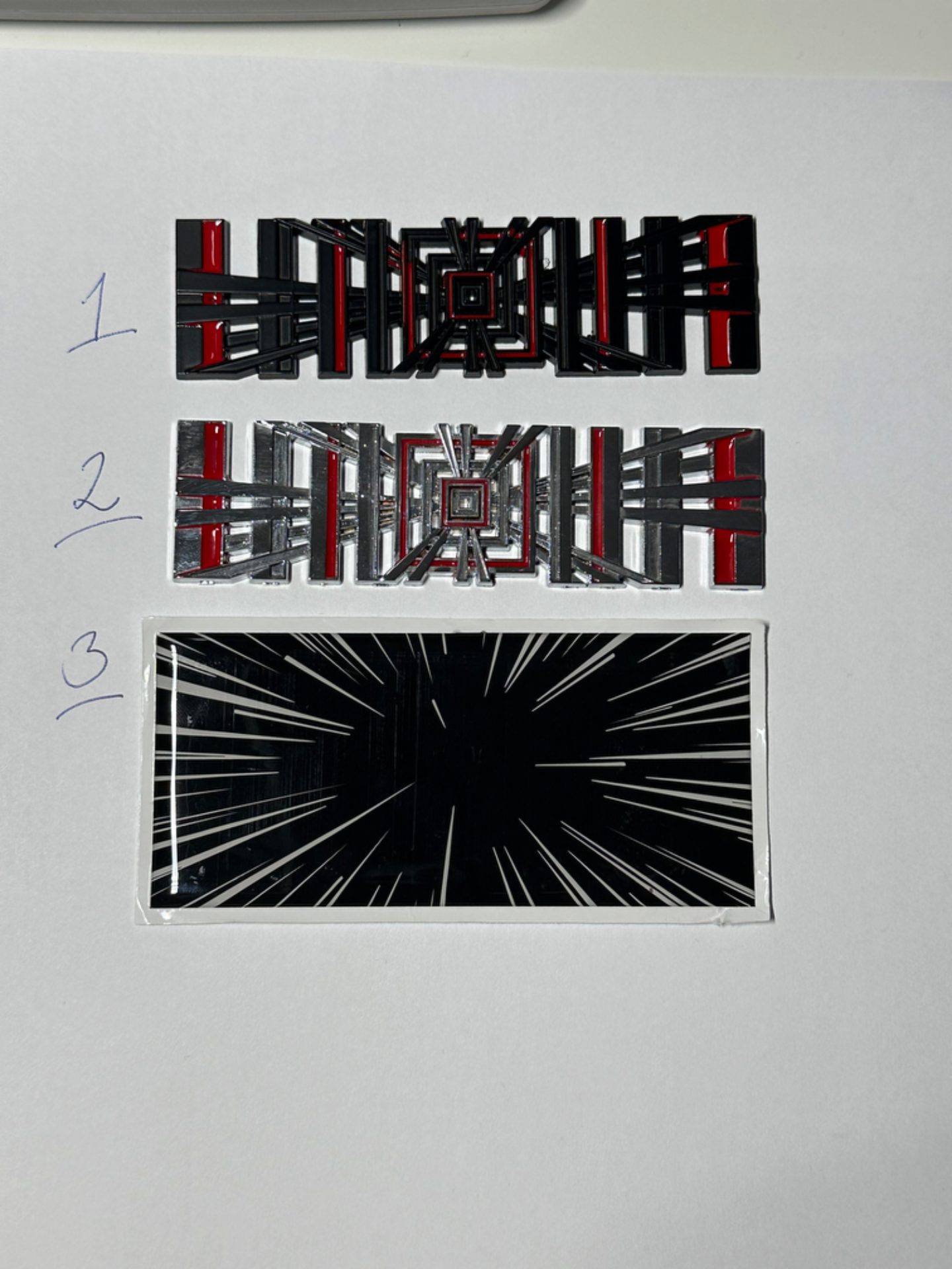 Plaid-emblem för Tesla i tre varianter – svart/röd, silver/röd och svart/vit